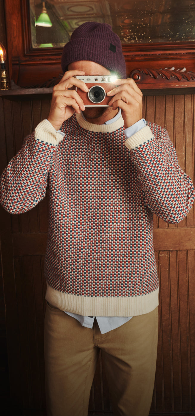 Man with a camera wearing Lambswool Seed Stitch Sweater.